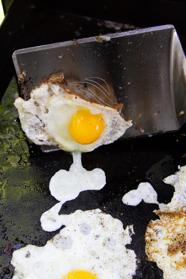 A very large metal spatula flipping over a fried egg.