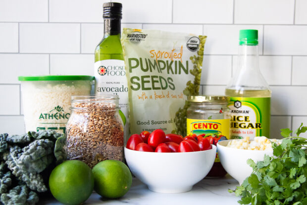 Ingredients for farro salad - farro grains, kale, limes, feta, oil, rice vinegar, cherry tomatoes, cilantro, frozen corn, and roasted red peppers.