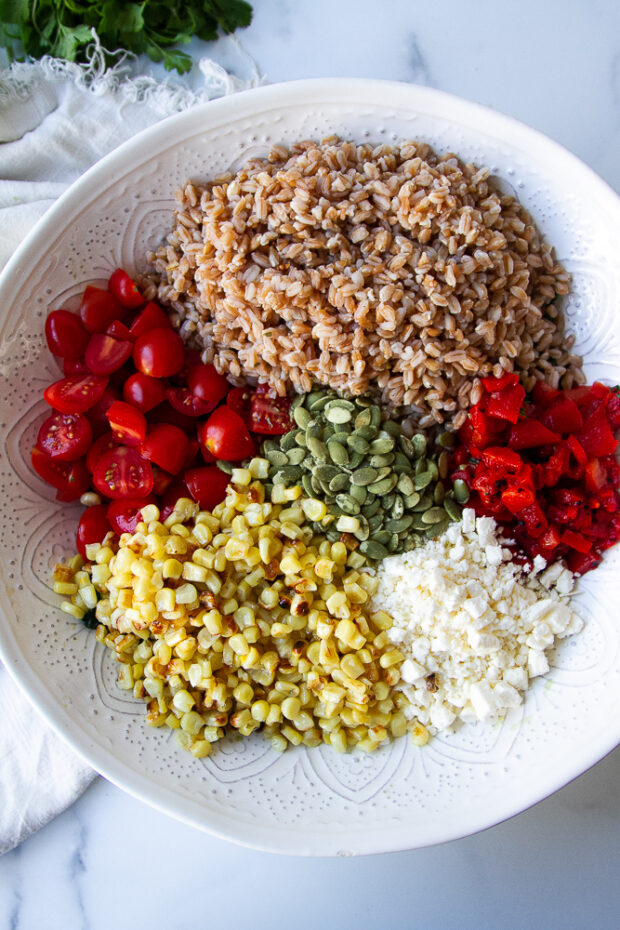 Same salad bowl with farro, cherry tomatoes, roasted red peppers, roasted corn, pepitas, and feat added.