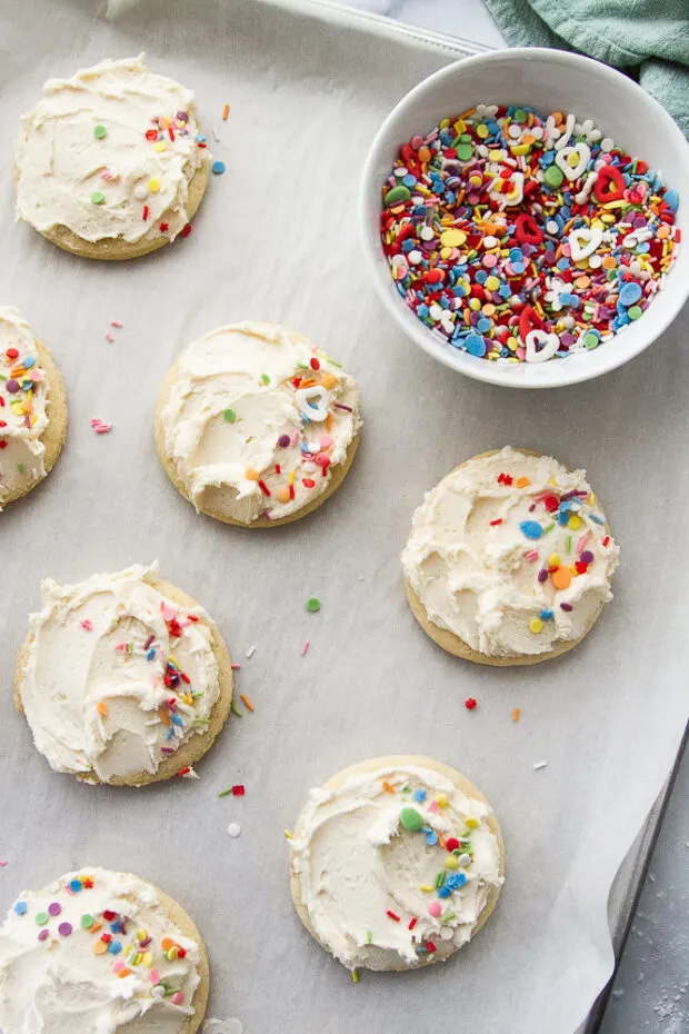 Frosted sugar cookies with multi-colored sprinkles next to a bowl of sprinkles.