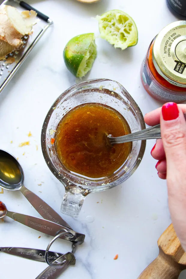 A small glass measuring cup with all of the ginger dressing ingredients added and whisked together with a fork.