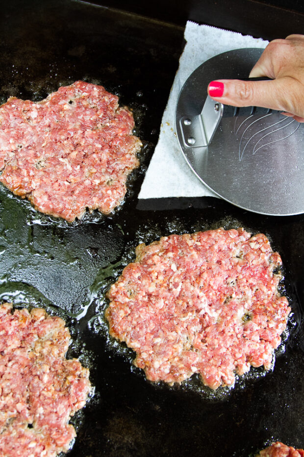 Burger patties on a griddle smashed with a burger smasher.