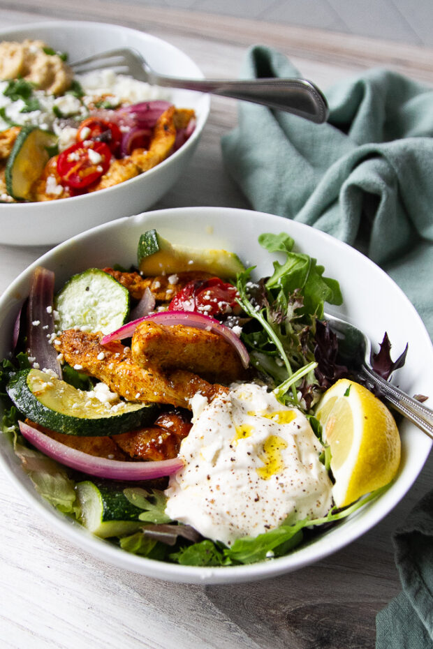 Bowl of chicken shawarma over salad greens with tahini yogurt dressing.