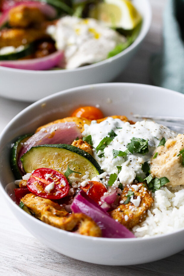 Roasted chicken shawarma and vegetables in a bowl with rice and tzatziki.