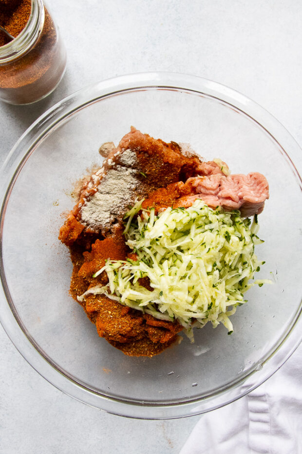 Glass bowl with ground turkey. Shredded zucchini, shawarma seasoning, and onion powder thrown on top.