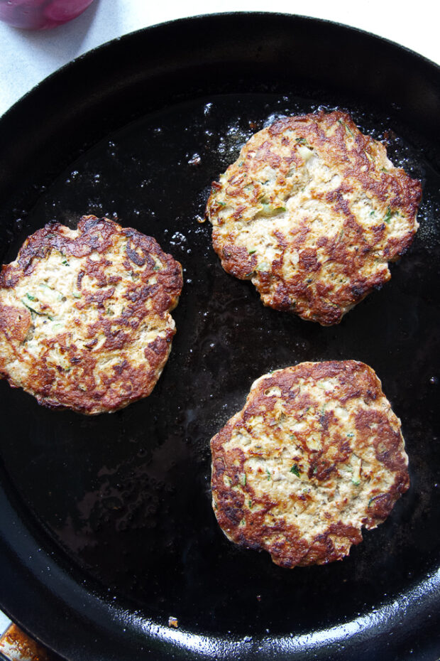 Three turkey patties cooking in a skillet.