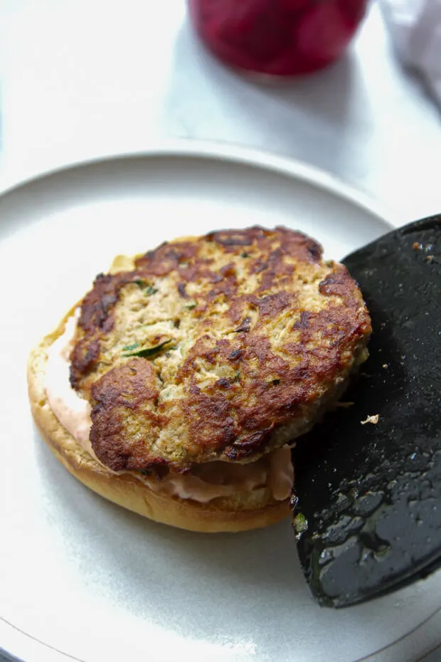 Cooked turkey patty placed on a bottom bun with some spicy mayo.