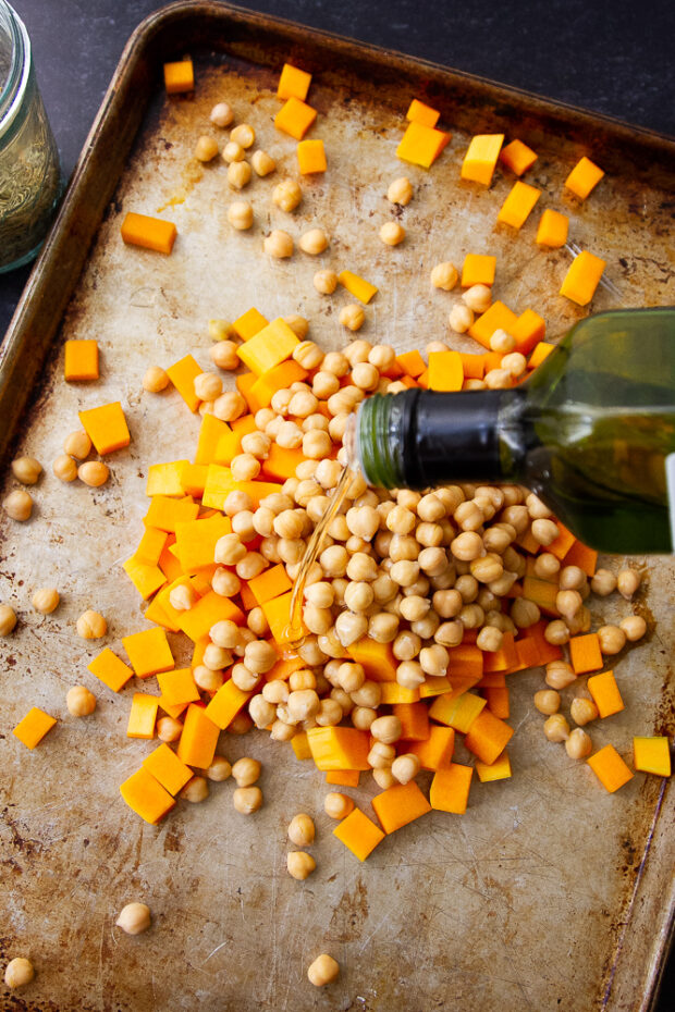 Butternut squash and chickpeas on a sheet pan with avocado oil being drizzled over the top.