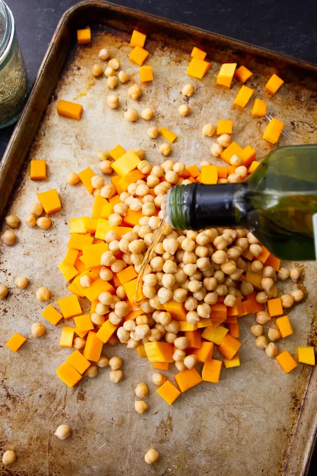 Butternut squash and chickpeas on a sheet pan with avocado oil being drizzled over the top.