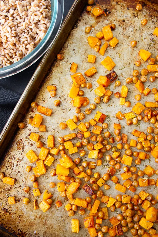 Finished roasted butternut squash and chickpeas on a sheet pan next to a bowl of cooked farro.