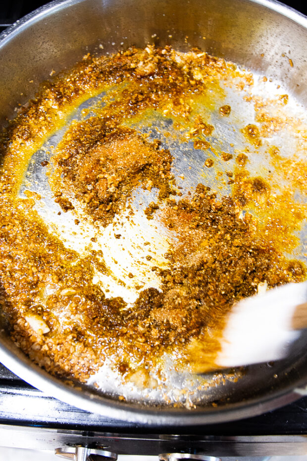 A deep skillet with dried onion, garlic, ginger, and spices frying up in some coconut oil. 