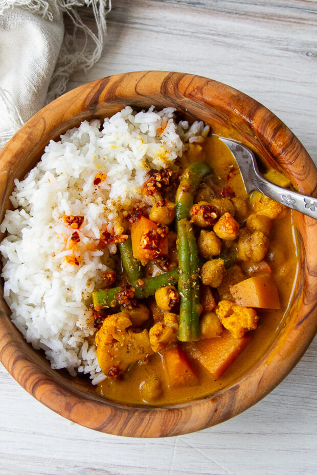 Another overhead shot of the curry in the wooden bowl with rice and some chili crunch on top.