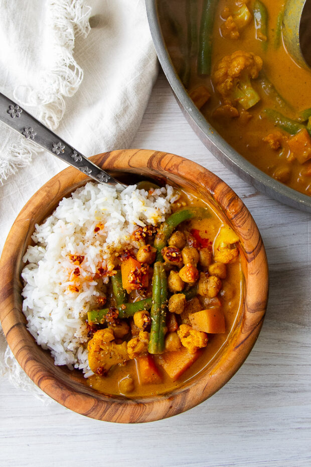 Bowl of curry with steamed rice next to the skillet of finished curry.