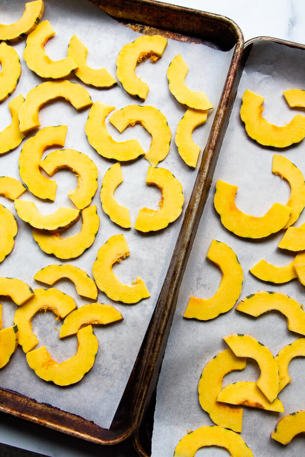 Squash slices divided between two parchment lined baking sheets. 