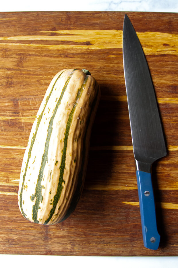 Cutting board with a whole delicata squash and a chef's knife.