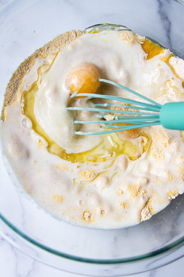 Clear bowl containing cornmeal, eggs, oil, and buttermilk.