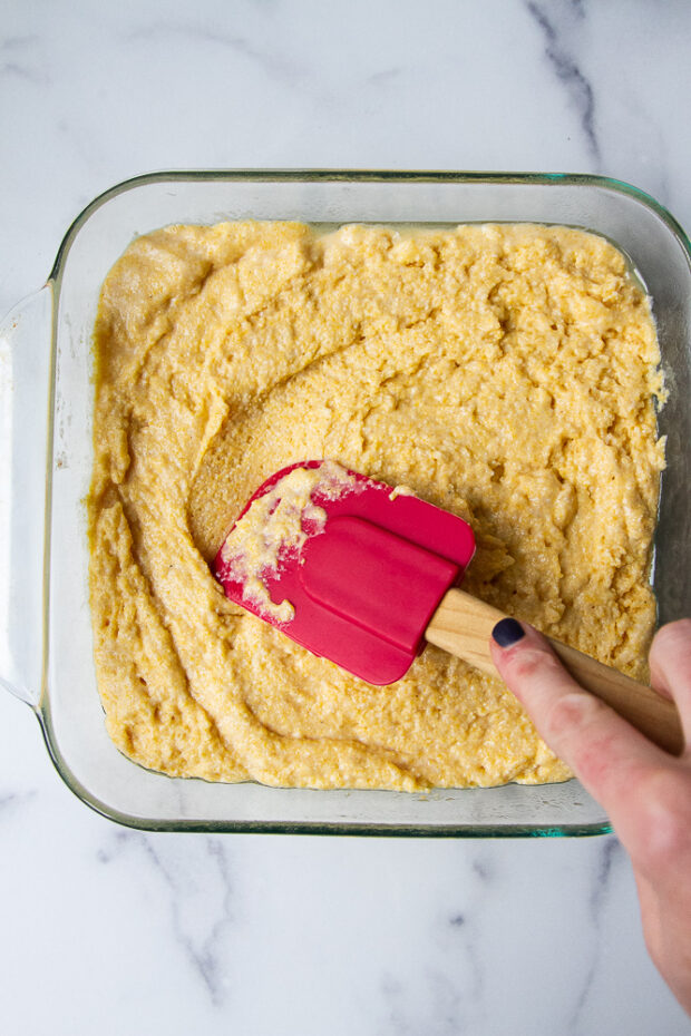 Cornbread batter pressed into a square baking dish.