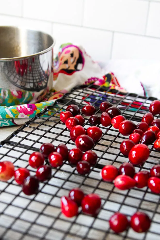 Making sugared cranberries by cooking the fresh cranberries in a simple syrup for a minute and now they're resting on a wire baking rack.