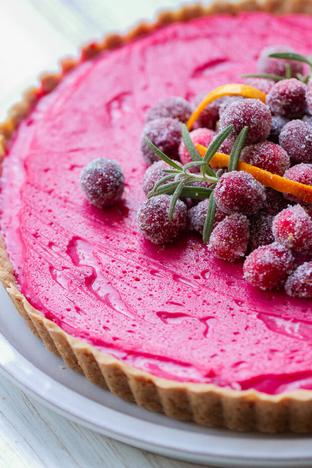 Finished cranberry tart topped with sugared cranberries, orange peel, and rosemary sprigs.