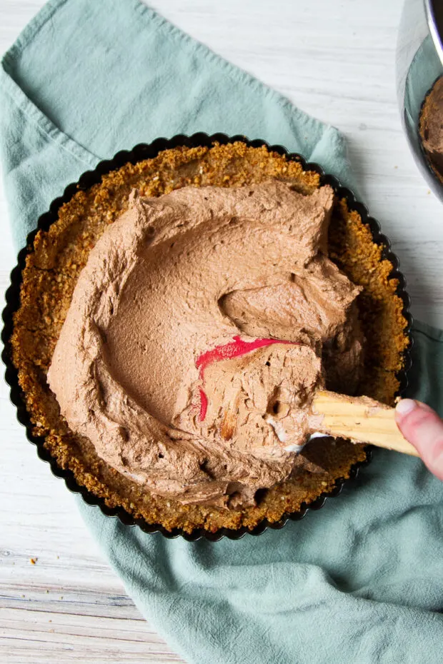 Chocolate mousse filling being spread into the baked pretzel tart crust. 