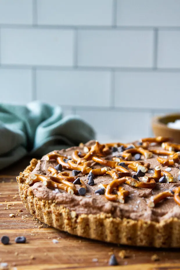 Nearly finished chocolate tart with all the garnishes: broken pretzels, sea salt flakes, and mini chocolate chips.