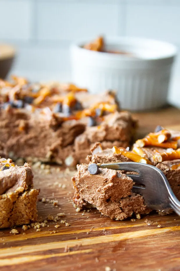 A fork taking a bite out of a slice of caramel chocolate tart. 